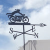 Motorcycle in the Wind Weathervane Silhouette of the "Motorcycle in the Wind Weathervane" by Black Fox Metalcraft Ltd against a cloudy sky, featuring directional letters S, W, E, and N.