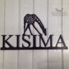 Laser Cut Metal Sign The Laser Cut Metal Sign by Black Fox Metalcraft Ltd features "KISIMA" and a giraffe silhouette, expertly crafted in steel and mounted on a light wood wall—perfect for creating a unique house name sign.