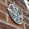 The Metal Art Address Signs from Black Fox Metalcraft Ltd feature handmade black and silver “23” numbers, mounted on a brick wall—an elegant option for anyone seeking custom metal address plaques.
