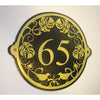 The Metal Art Address Signs by Black Fox Metalcraft Ltd feature a round black and gold design with the number 65, elegant floral details, and two birds—an ideal choice to add charm to your home’s exterior. Painted by hand in gold.