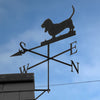 Basset Hound weathervane mounted to the gable end of a garage, with blue sky background.