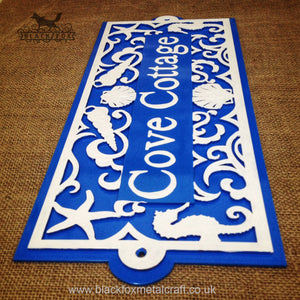 Metal art address sign, powder coated bright blue, with intricate laser cut detailing in white and text painted by hand.