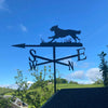 Flat Coated retriever weathervane depicts the dog running through long grass. Blue sky background.