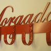 A red Industrial Style Coat Hooks rack by Black Fox Metalcraft Ltd with "Morada" in cursive above four riveted metal hooks, mounted on a cream-colored wall.