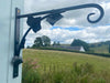 A hand made hanging basket bracket featuring forged ivy leaves, pictured in the Scottish borders countryside.