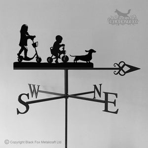 Introducing the expertly crafted Children on Bikes Weathervane by Black Fox Metalcraft Ltd, showcasing a charming silhouette of two children riding scooters with a playful dog, complete with rust protection and oriented to point northeast.