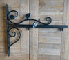 Elegant black metal wall bracket featuring decorative scrolls and leaf accents, ideal for displaying the Black Fox Metalcraft Ltd Roe Deer Hanging Sign or any handcrafted steel sign. Shown on a wooden surface, this bracket enhances woodland-themed metal sign displays with sophisticated charm.