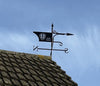 The Bespoke Crest Weathervane by Black Fox Metalcraft Ltd, featuring the Leeds United logo and directional markers, sits atop a tiled roof against a clear blue sky.