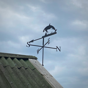 Weathervane featuring an Orca mounted to the end of a garage, photographed with blue sky background.