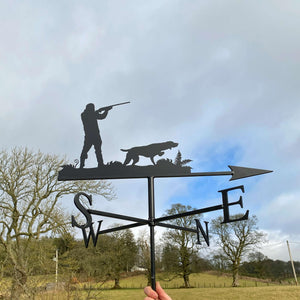 Shooting weathervane featuring beautiful intricate fern design, showing a man aiming his gun, while his Pointer dog awaits instruction. Photographed in Scottish countryside.