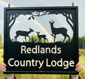 Hanging sign featuring three Roe Deer, with a dark sky and rainbow in the background of the photo.