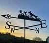 Against the backdrop of a sunset sky, the silhouette of the Spaniel Flushing Pheasants Weathervane by Black Fox Metalcraft Ltd features elegantly perched birds. Compass directions—NSEW—are clearly visible. This weathervane not only exudes charm but also includes rust protection, making it an ideal gift for those in the countryside.