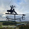 The Dancing Couple Weathervane by Black Fox Metalcraft Ltd features two dancers' silhouettes set against a cloudy sky, rural fields, and buildings. "Tango Dancers" appears in the lower left corner of the image.