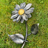 The Forged Metal Flower by Black Fox Metalcraft Ltd, featuring silver petals and a gold center, lies on green grass like a gilded daisy ornament.