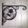 Black Fox Metalcraft Ltd's Bumble Bee Hanging Basket Bracket is a hand-forged, elegant, and sturdy wrought iron wall bracket with a charming bee design, perfect for enhancing home decor when mounted on a white wooden wall.